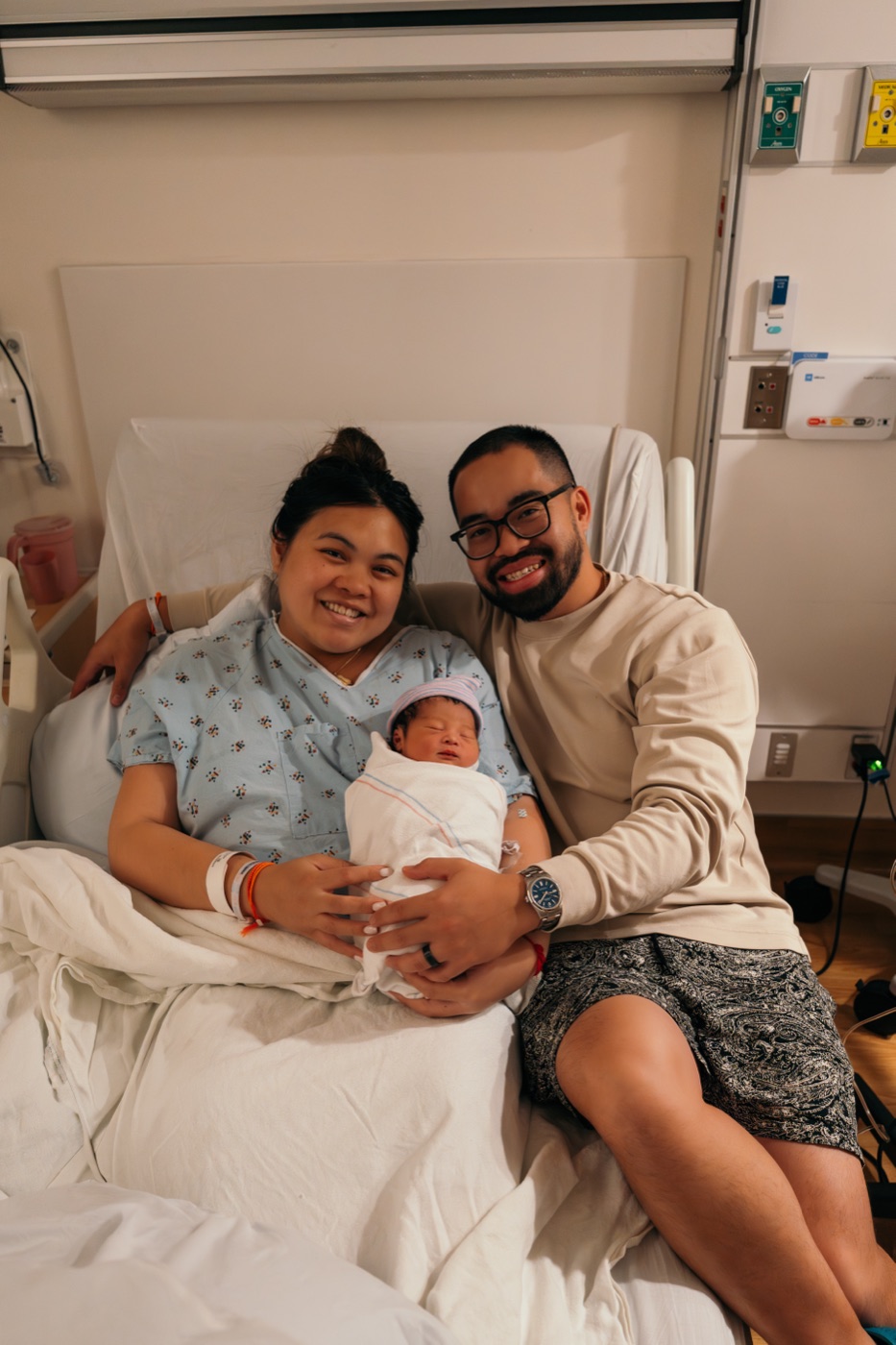 Debra and Vinh smiling in a hospital room, holding their newborn